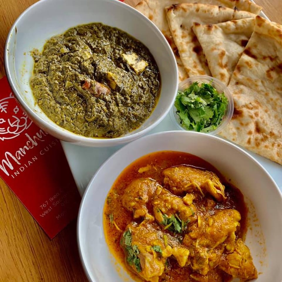 Two bowls of Indian curry, one green and one orange, with naan bread and cilantro.
