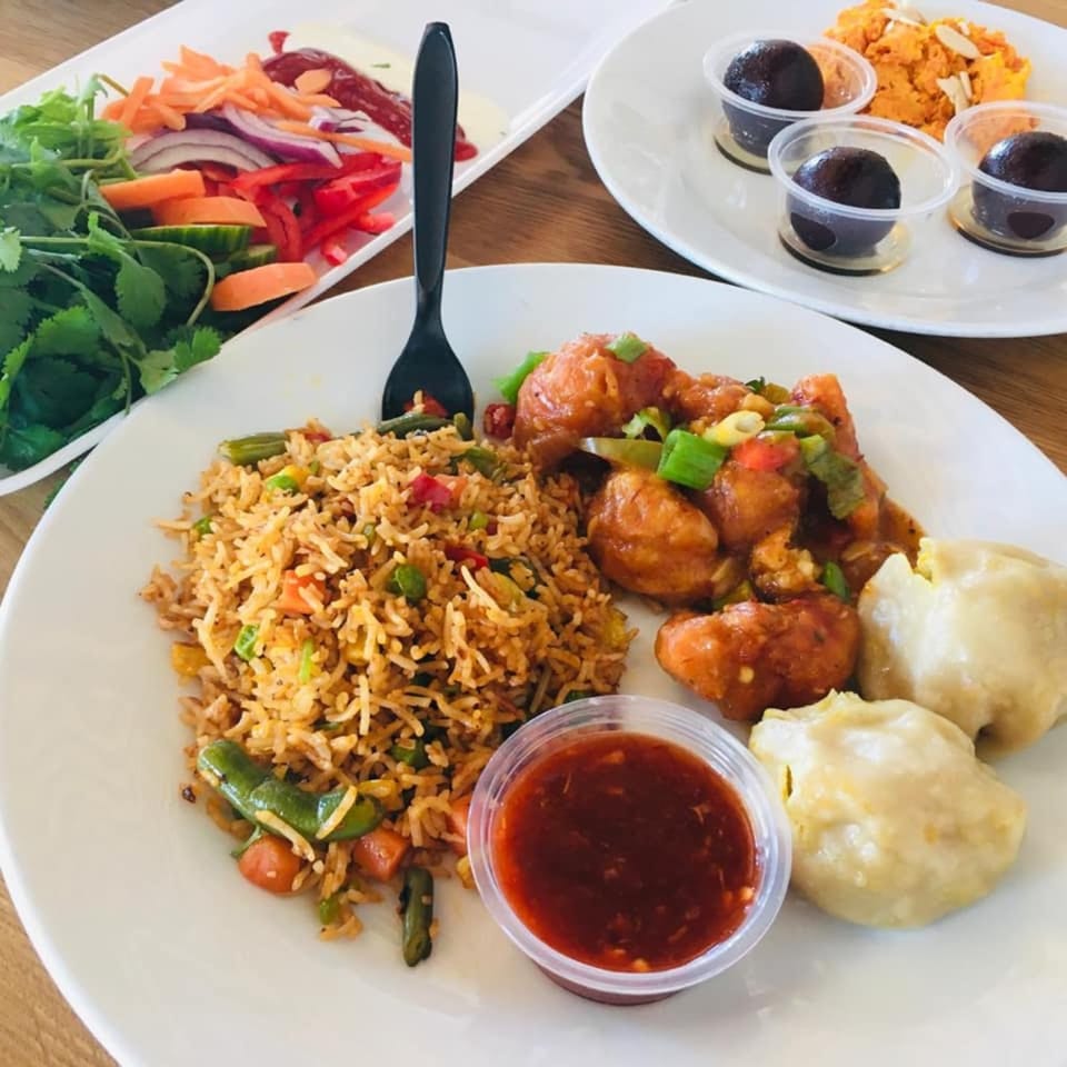A plate of fried rice, orange chicken, dumplings, and chili sauce, with salad and desserts.