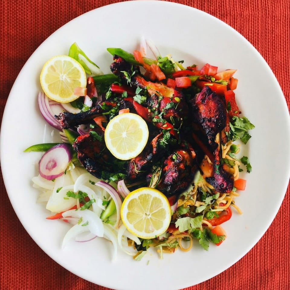 Tandoori chicken drumsticks with noodles, red onions, bell peppers, cilantro, and lemon slices.